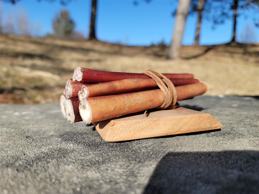 Bundle of thick straight bully sticks tied with a leather strap on a wooden board